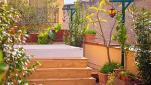 Un patio con escalones que conducen a una terraza, rodeado de plantas en macetas y un farol colgante.