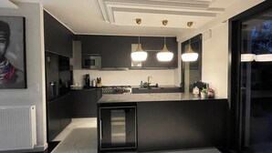 Une cuisine moderne avec des meubles de couleur sombre, un îlot central et des luminaires suspendus.
