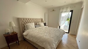 Une chambre à coucher avec un grand lit, une table de chevet avec une lampe et une vue sur l’extérieur par une fenêtre.