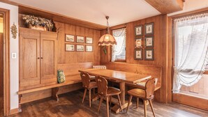 A wooden dining room with a large table and four chairs, framed pictures on the walls, and a hanging light fixture. - Casa Funivia 2, close to the cable car and the center (Cortina d´Ampezzo)