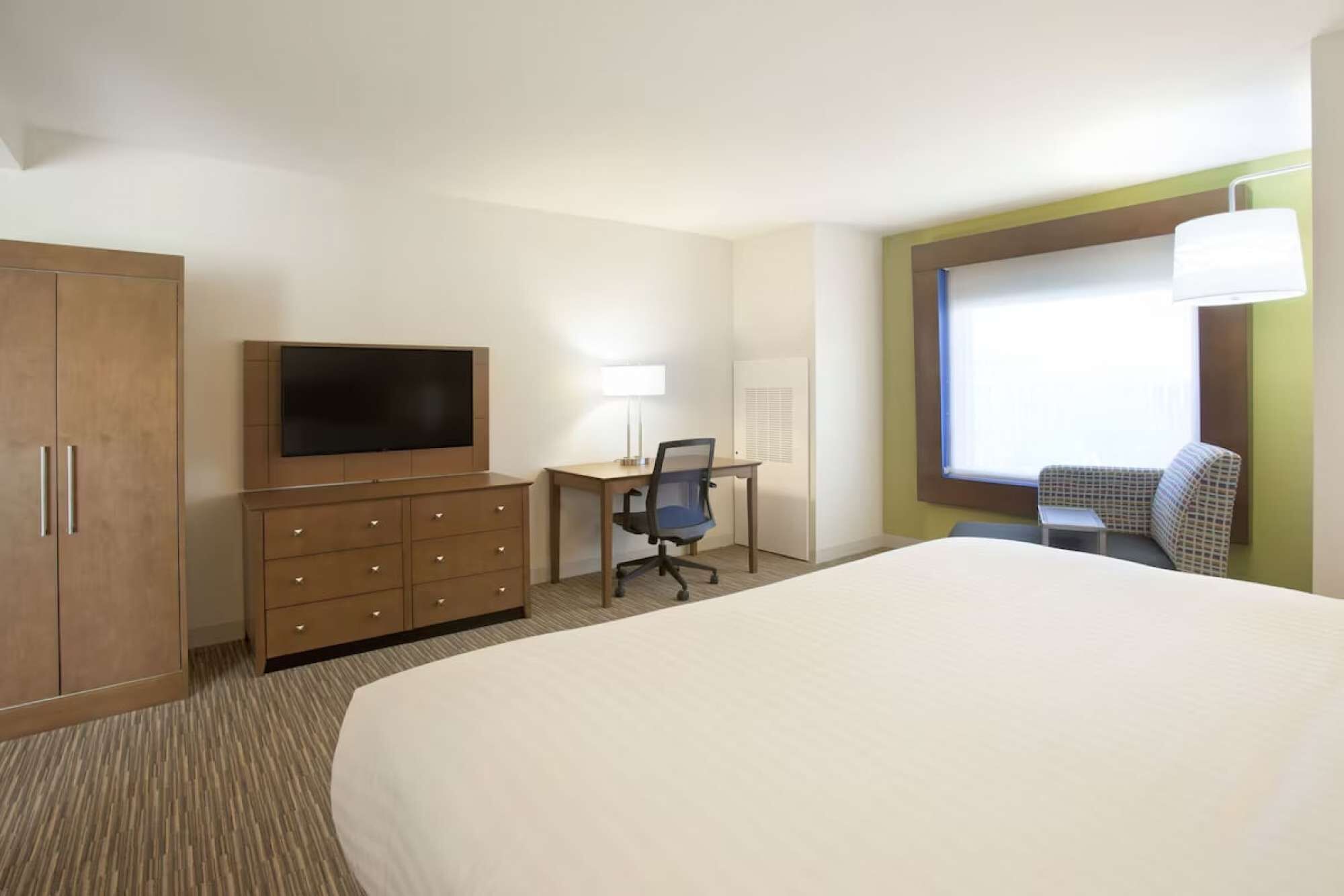 Une chambre d’hôtel avec un grand lit, un bureau avec une chaise, une télévision et une fenêtre donnant sur un beau paysage.