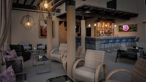 Un espace lounge moderne avec des meubles en osier, un bar agrémenté d'une enseigne au néon et une grande fenêtre donnant sur la ville.