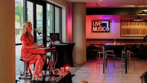 Une personne joue du clavier dans une pièce où l’on peut voir un panneau indiquant « MUSIQUE EN DIRECT », ainsi que des tables et des chaises.