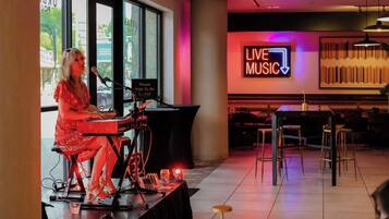 Een persoon speelt op een keyboard in een kamer met een bord waarop 'LIVE MUSIC' staat, tafels en stoelen.