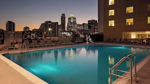 Une piscine sur le toit offrant une vue sur les toits de la ville, des chaises longues et un bâtiment moderne en arrière-plan.