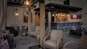 A modern lounge area with wicker furniture, a bar with a neon sign, and a large window overlooking the city. - Near Texas Capitol + Rooftop Pool. Bar. Dining. (Austin)