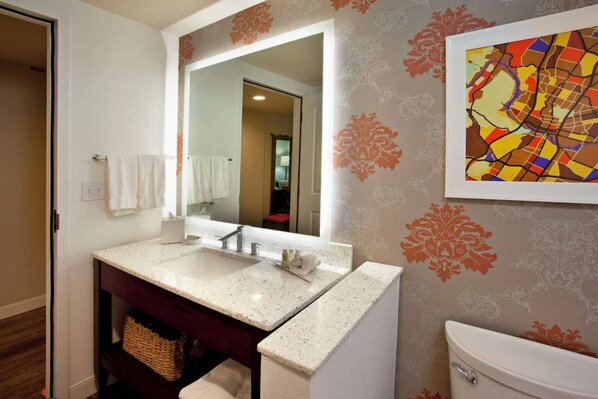 Une salle de bain avec un lavabo blanc, un miroir et des toilettes. Un mur décoratif présente des motifs floraux et une peinture abstraite aux couleurs vives.