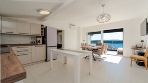 Una cocina moderna con armarios blancos, un comedor con mesa y sillas, y un ventanal con vistas al mar.