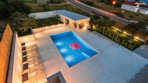 Una piscina con una decoración de flamenco rosa, rodeada por un porche cubierto con iluminación exterior.
