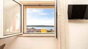 Una habitación con ventana que da a un lago y edificios, un televisor de pantalla plana montado en la pared, y un objeto amarillo en el alféizar.