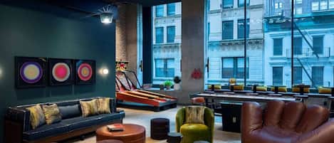 A modern lounge area with a sofa, ottomans, a leather armchair, and a dartboard.