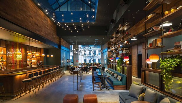Een ruime bar met zitplaatsen, een hoge plafond en uitzicht op de skyline.