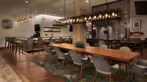 Une cuisine et une salle à manger modernes, avec une longue table en bois, des chaises grises et des luminaires suspendus.