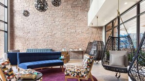 A modern lounge area with a brick wall, a blue sofa, patterned chairs, a hanging chair, and a small table with a basket.