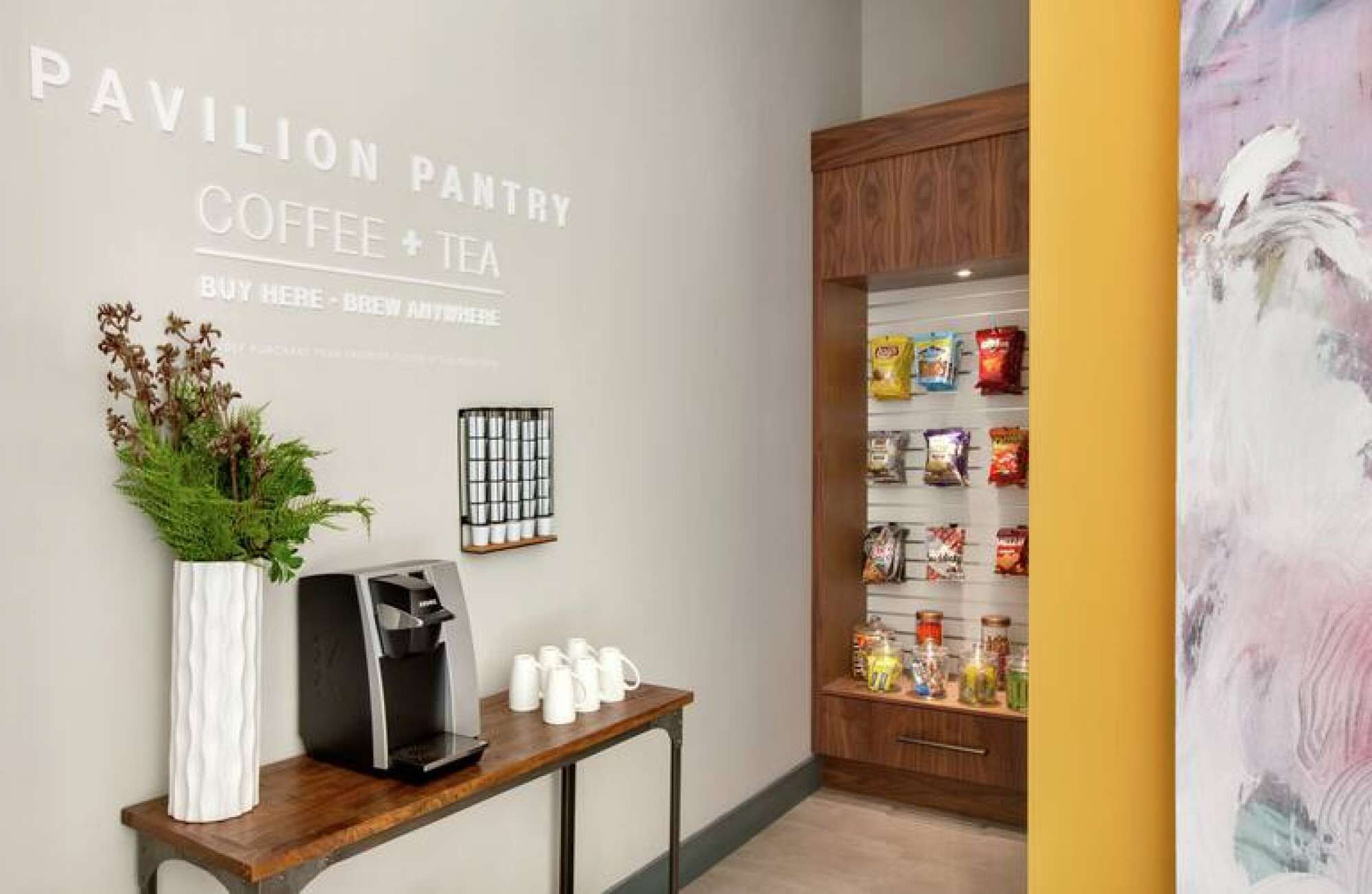 A coffee and tea station with a coffee machine, cups, and a display of snacks.