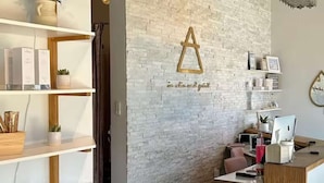 A reception area with a white brick wall, a wooden reception desk, and shelves with various items. - CU Game Days | Restaurant + Mobility Access Room (Boulder)