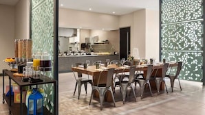 A modern dining area with a long table and chairs, a kitchen in the background, and decorative screens. - CU Game Days | Restaurant + Mobility Access Room (Boulder)