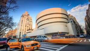 A modern building with a unique circular design, located in an urban setting with tall buildings around.