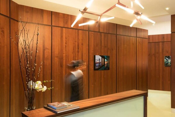 Un espace d’accueil avec un lambris en bois, un vase orné de branches et de fleurs, et un tableau encadré accroché au mur.