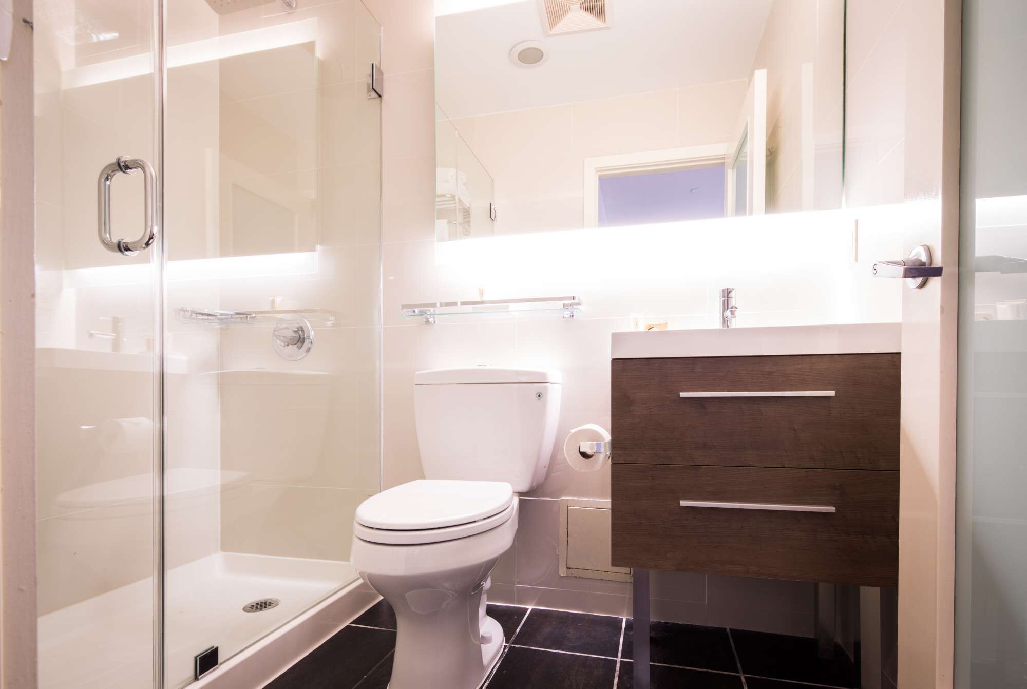 Une salle de bain moderne avec une douche à parois de verre, des toilettes blanches et un meuble-lavabo en bois avec un miroir.