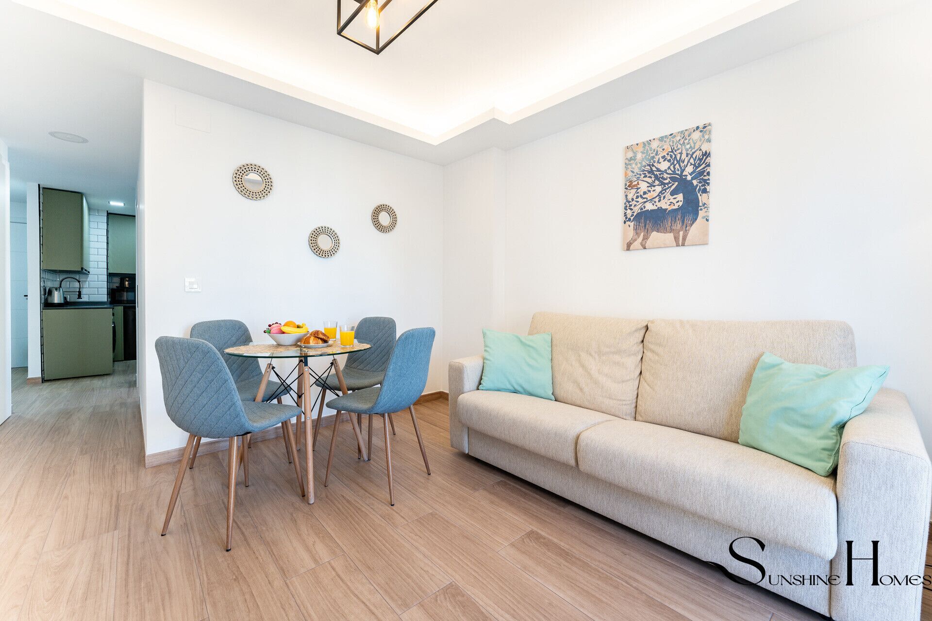 Ein modernes Wohnzimmer mit einem beigefarbenen Sofa, blauen Sesseln und einem Glastisch mit Frühstücksgebäck.