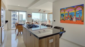 A modern kitchen with a central island, large windows, and a city view. - Stunning Ocean+Marina Views Rooftop Infinity Pool (Puerto Vallarta)