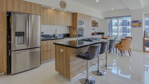 A modern kitchen with a central island, stainless steel appliances, and a dining area with bar stools. - Stunning Ocean+Marina Views Rooftop Infinity Pool (Puerto Vallarta)