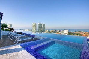 Piscina infinita no terraço com espreguiçadeiras e vista para a cidade.