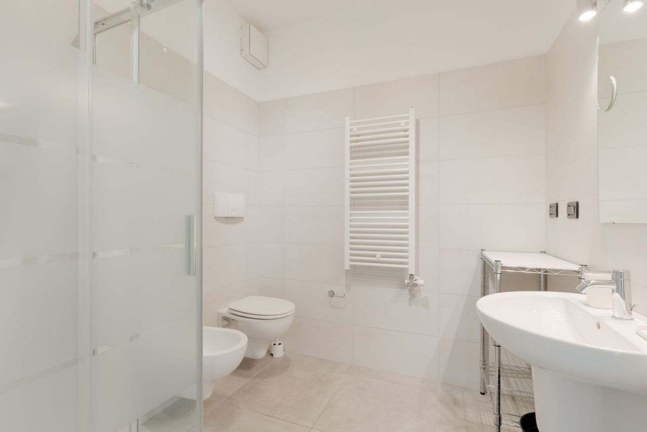 A modern bathroom with a glass shower enclosure, a toilet, a towel rack, and a sink.