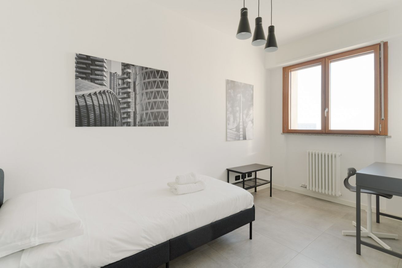 A modern bedroom with a bed, a small table, a radiator, and artwork on the wall.