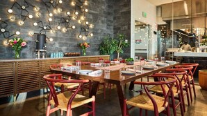 A dining area with a long wooden table, red chairs, and a modern wall with hanging lights. - In The Heart of Boston’s Seaport + Rooftop Bar (Boston)