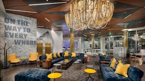 A modern lobby with a marble wall, blue sofas, yellow chairs, and a large chandelier. - In The Heart of Boston’s Seaport + Rooftop Bar (Boston)