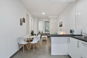 Eine moderne Küche mit weißen Schränken, einem Essbereich mit rundem Tisch und Stühlen sowie einer kleinen Kücheninsel mit Spüle.