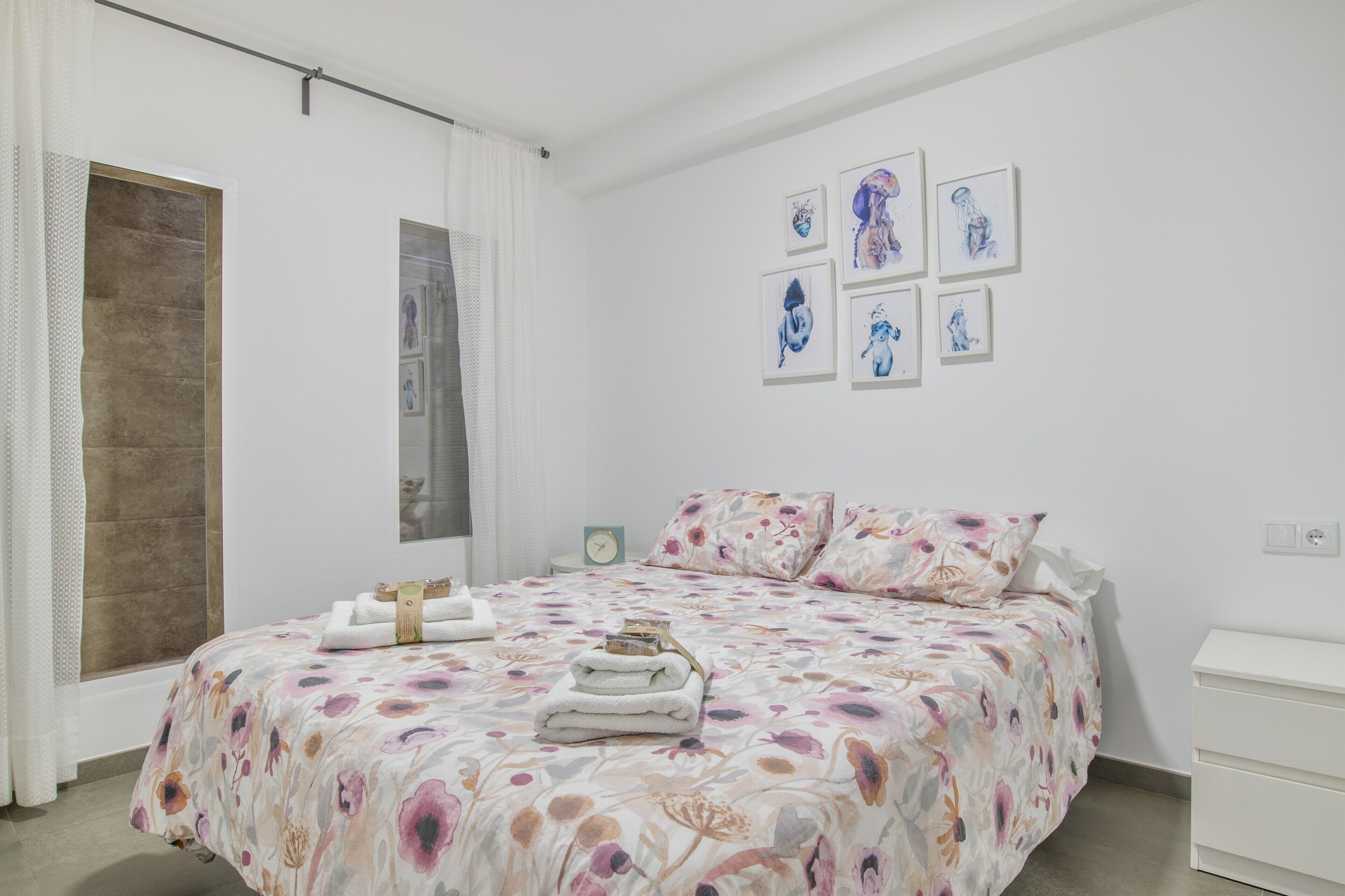 Een slaapkamer met een bed, nachtkastje, een wandklok en kunst aan de muur.