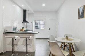 Una cocina moderna con armarios blancos, una campana extractora negra, un microondas y dos taburetes de bar.