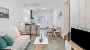 Een moderne woonkamer met een bank, salontafel, televisie, en een eethoek met stoelen en een tafel.