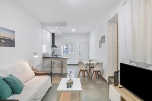Ein modernes Wohnzimmer mit einer Couch, Couchtisch, Fernseher und einem Essbereich mit Stühlen und Tisch.