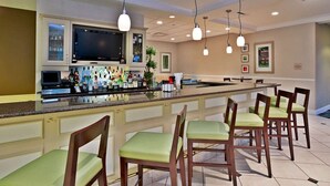 A bar area with a long counter, multiple bar stools, and overhead lighting. - Steps to Fountain Walk + On-site Dining. Pool. Gym (Novi)
