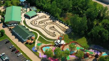 An aerial view of a theme park with a winding roller coaster, a large dome structure, and a parking lot.