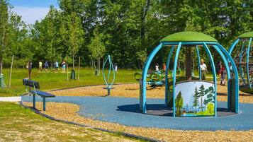 A playground with a bench, swings, and a covered play area with a forest mural.