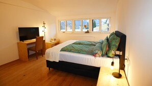 Un dormitorio con cama, escritorio, televisor y ventana con vistas al exterior.
