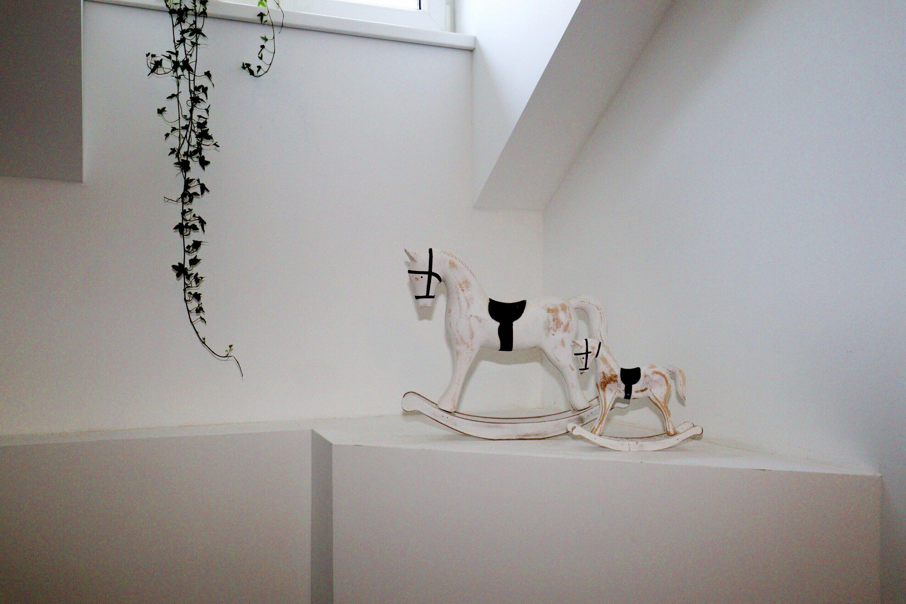 A white wall with a white sculpture of a horse and a vine hanging from the ceiling.