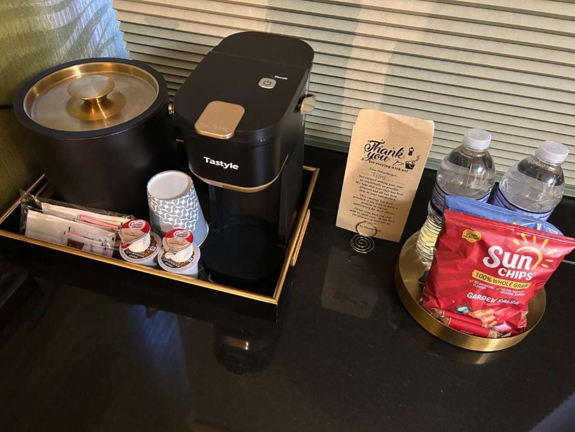 Tray with coffee maker, cups, snacks, and bottled water on the counter.