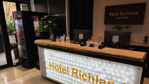 Een receptiebalie met een bordje waarop 'Hotel Richland' staat en een bord erboven met de tekst 'Hotel Richland New York'.