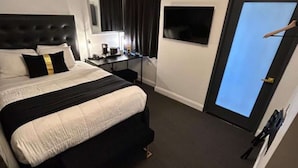 A hotel room with a bed, a desk, a chair, a dresser, a mirror, a door, and a window.