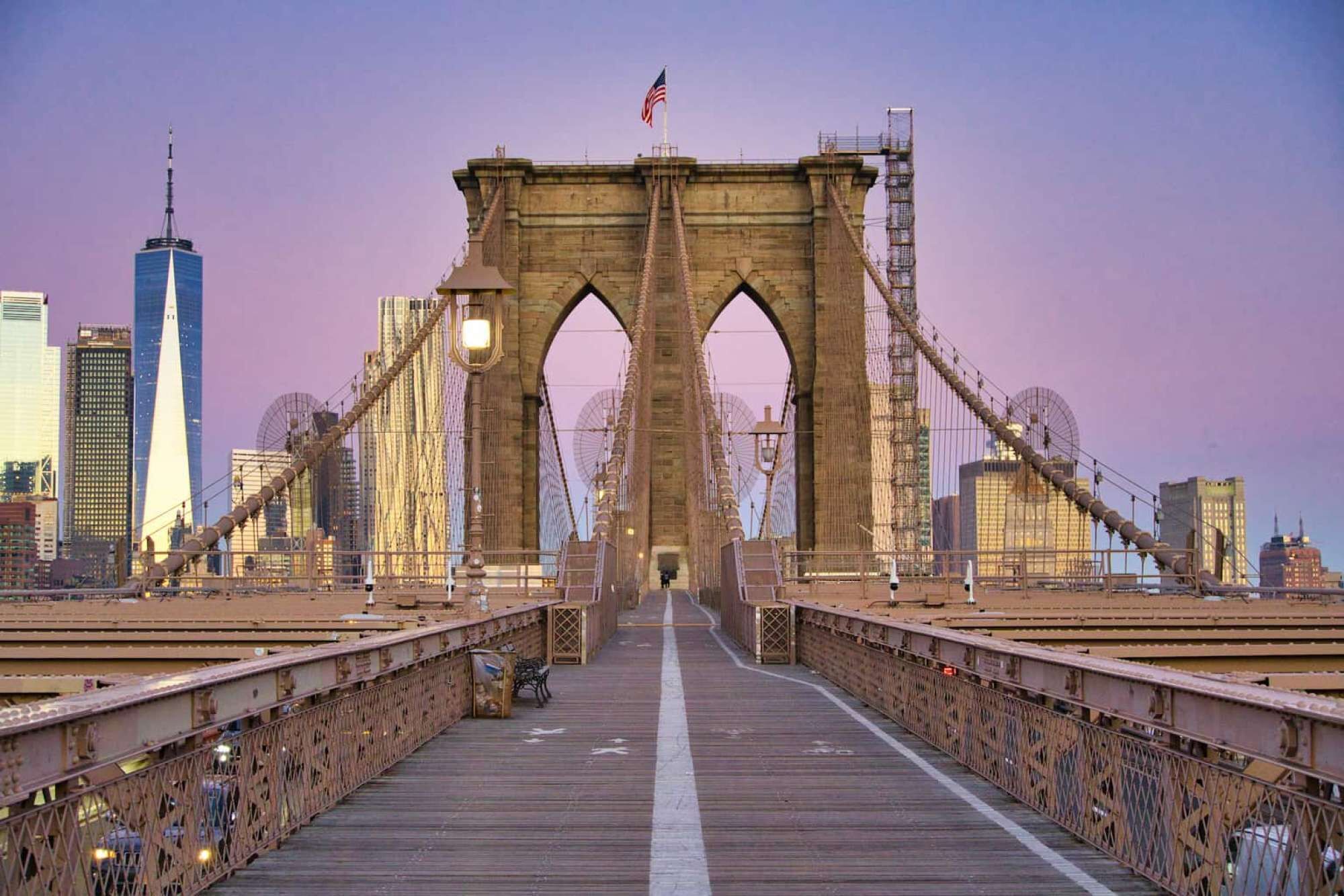 A bridge with a central arch and two towers, with a city skyline in the background.