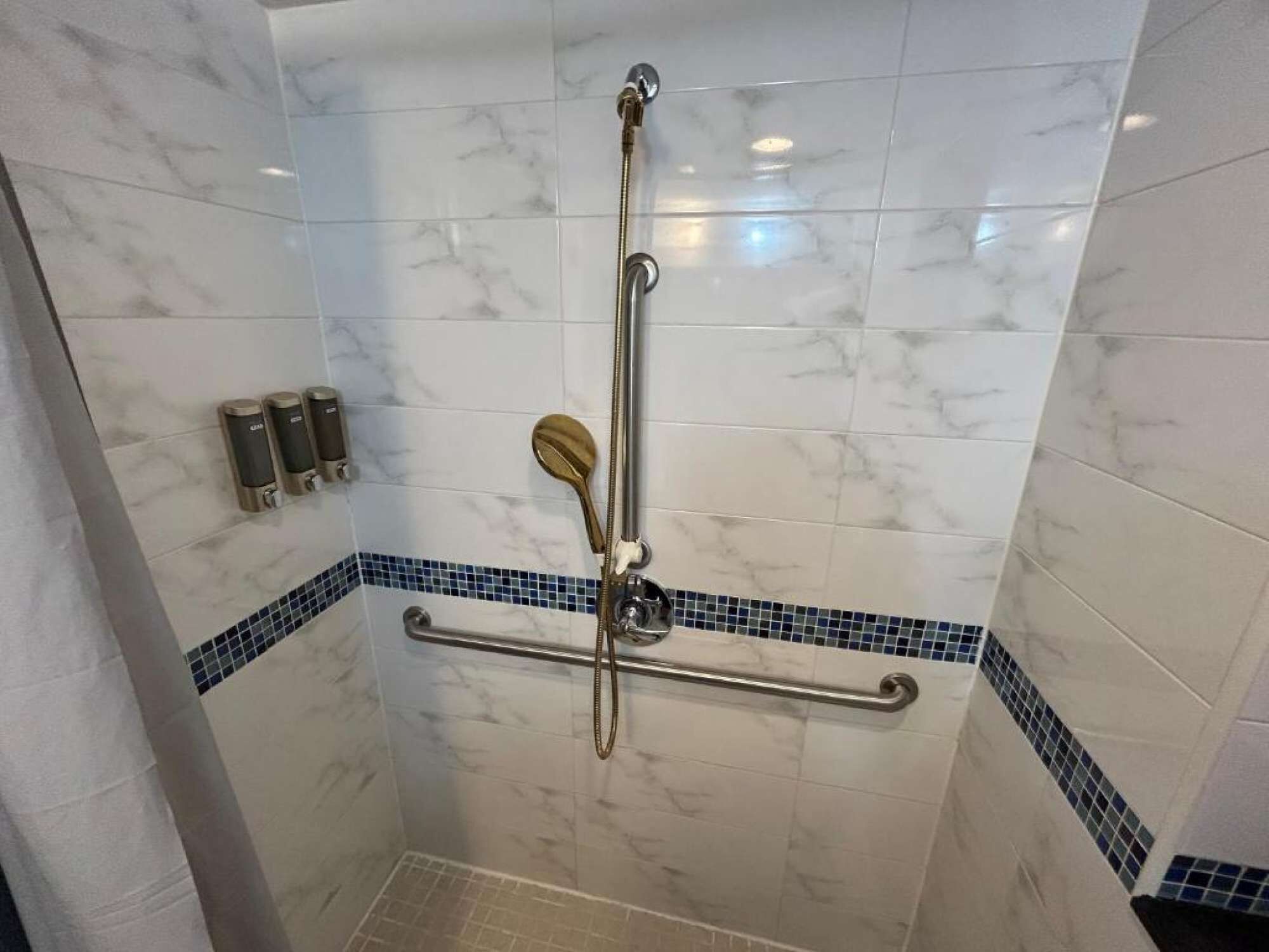 Shower with grab bars, tiled walls, and mounted dispensers for daily use.