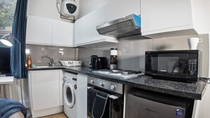 A compact kitchen with a microwave, toaster, coffee maker, and a washing machine. - Spacious Charming Studio in Birmingham (Birmingham)