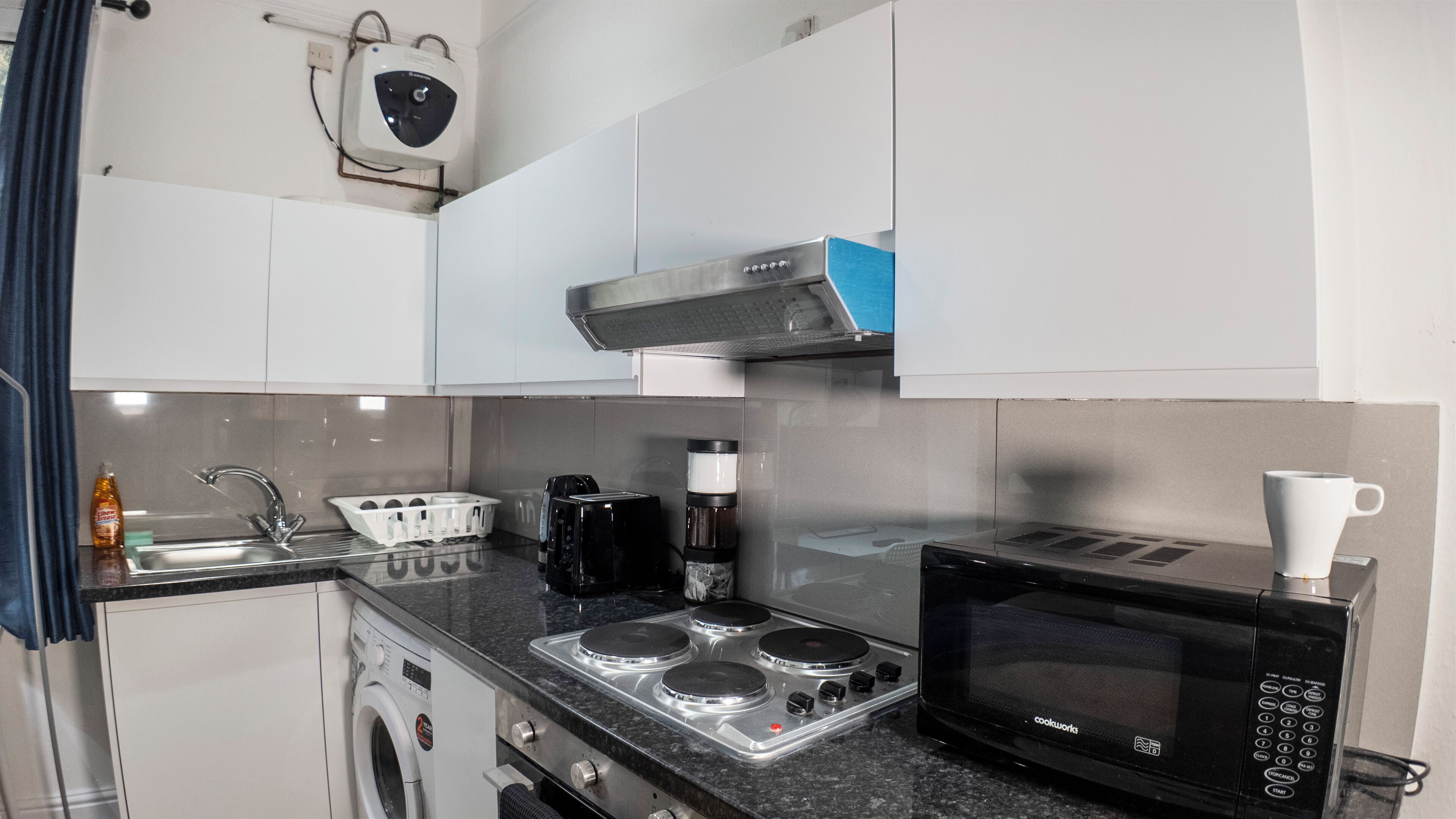 Une cuisine compacte équipée d’un lave-linge intégré, d’une cuisinière à quatre brûleurs, d’un four à micro-ondes et d’une machine à café.
