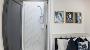 A bathroom with a shower, a bed with pillows, and two framed artworks on the wall. - Spacious Charming Studio in Birmingham (Birmingham)